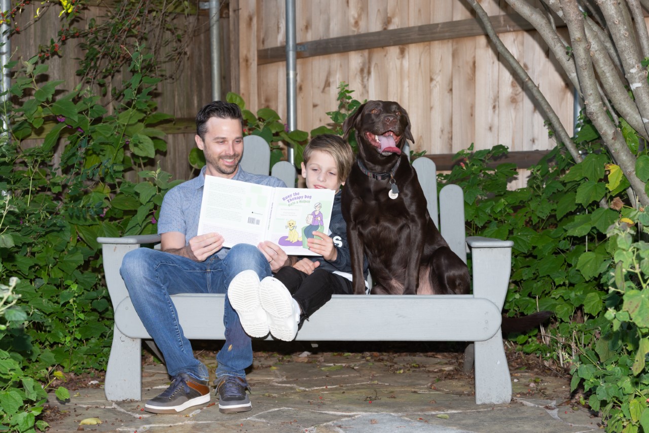 photo of a child and young adult reading a book with a Labrador retriever by their side